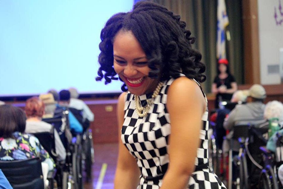 New York Cares volunteer smiles behind a crowd of residence from the new Jewish Home celebrating Older American Month