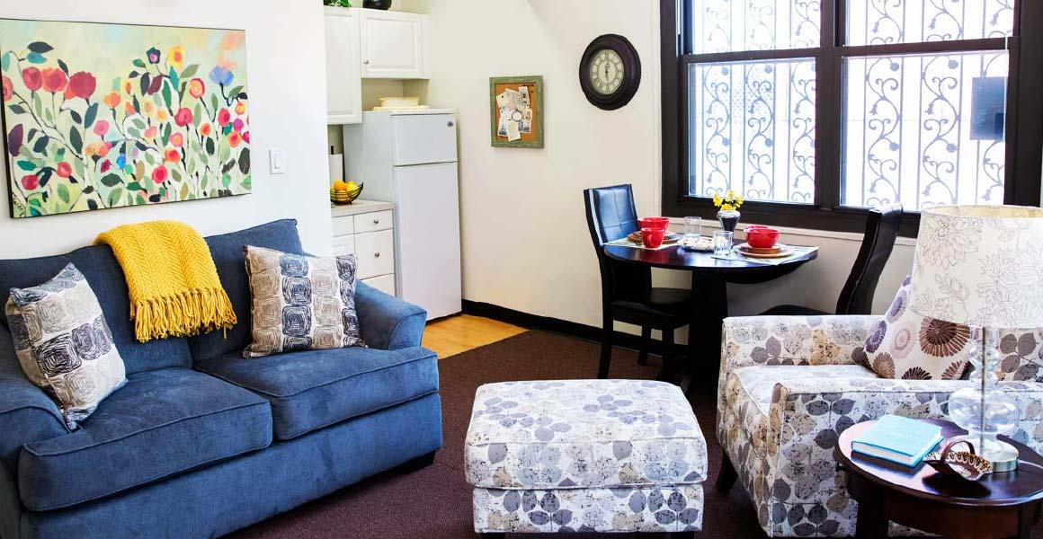 Blue couch with a bright yellow blanket draped on top across from a floral pattern love seat at the Kittay Senior Apartment