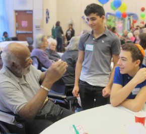 Two young volunteers at The New Jewish Home talk to an older African American man sitting in a chair