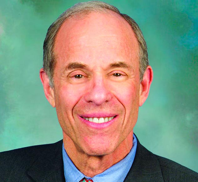 Richard Eisner A middle-aged man with short, thinning hair smiles while posing for a headshot in front of a green backdrop. He wears a dark suit jacket, a light blue dress shirt, and an orange tie.