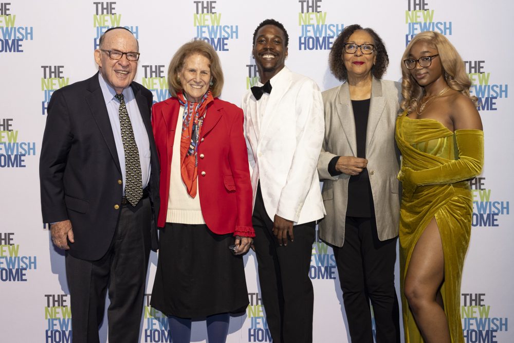 Five people stand together, smiling, in front of a backdrop that reads 