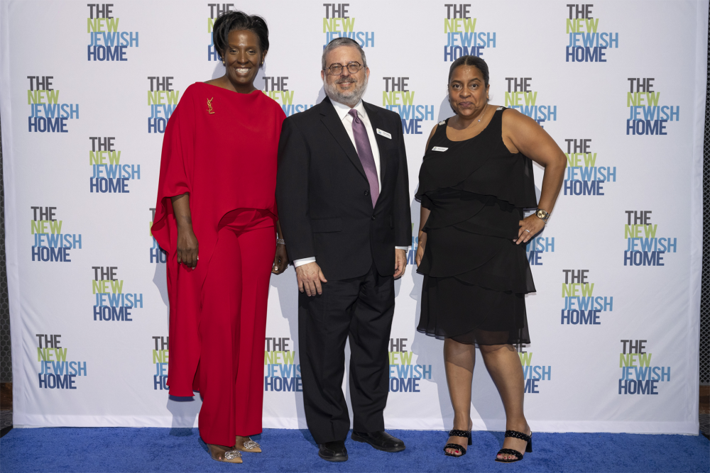 Three people pose and smile on a blue carpet in front of a backdrop with 