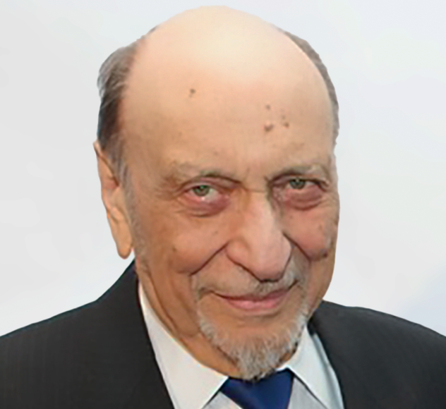 MiltonGlaser-p An elderly man with a receding hairline, light skin, and a short gray goatee, wearing a dark suit, white shirt, and blue tie, smiles slightly against a plain, light background.
